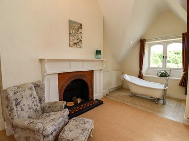 A room with a floral armchair and footstool next to a white fireplace and a clawfoot bathtub by a window at North Wing in Middleton Hall Estate near Belford
