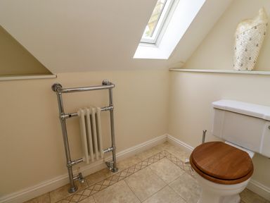 A bathroom with a toilet with wooden seat and a chrome towel radiator under a skylight window at North Wing in Middleton Hall Estate near Belford