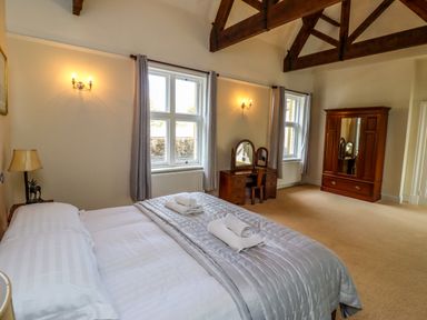 A bedroom with a bed and towels a wooden dressing table and a wardrobe with exposed wooden beams at North Wing in Middleton Hall Estate near Belford