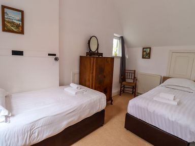 A bedroom with two single beds a wooden wardrobe a chair and framed pictures on the walls at North Wing in Middleton Hall Estate near Belford