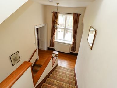 A staircase with carpet leading down to a wooden floor area with a window and brown curtains at North Wing in Middleton Hall Estate near Belford