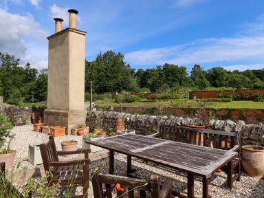 An outdoor seating area with wooden table and chairs surrounded by potted plants and a stone wall at North Wing in Middleton Hall Estate near Belford