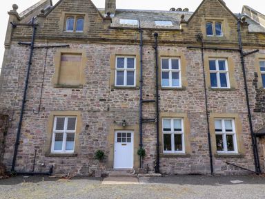 A stone building with multiple windows and a white door at North Wing in Middleton Hall Estate near Belford