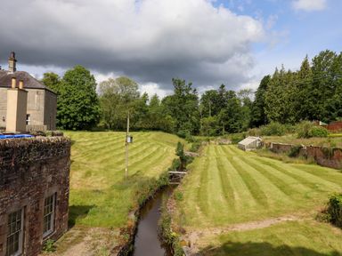 A garden with striped mowed grass a small stream greenhouse and trees at North Wing Middleton Hall Estate near Belford