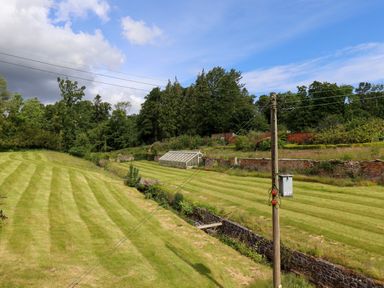 A grassy field with stripes a stone wall a greenhouse trees and a wooden utility pole with wires at North Wing in Middleton Hall Estate near Belford