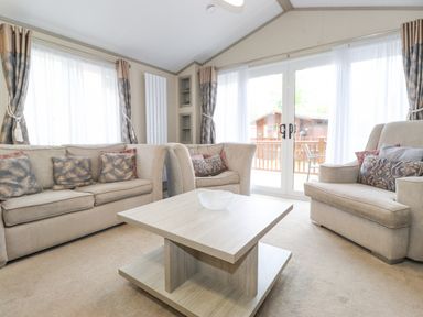 A living room with beige sofas and a wooden coffee table near glass doors at Tawny Owl Lodge in Coniston 4 White Cross Bay near Windermere