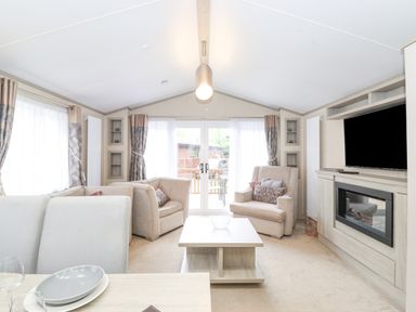 A living room with two armchairs a coffee table and a television above a fireplace at Tawny Owl Lodge in Coniston 4 White Cross Bay near Windermere