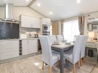 A kitchen and dining area with a table set for six and modern appliances at Tawny Owl Lodge Coniston 4 White Cross Bay near Windermere