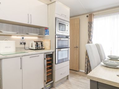 A kitchen area with a toaster bread box microwave ovens and dining table with chairs at Tawny Owl Lodge Coniston 4 White Cross Bay near Windermere