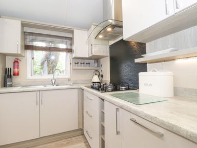 A kitchen with a sink under a window a gas stove bread box and kitchen cabinets at Tawny Owl Lodge Coniston 4 White Cross Bay near Windermere