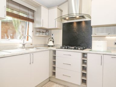 A kitchen with a gas stove a kettle a bread box and glass jars on shelves at Tawny Owl Lodge Coniston 4 White Cross Bay near Windermere
