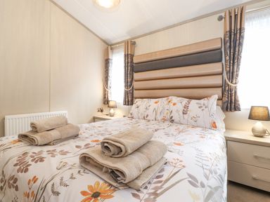 A bedroom with a double bed floral bedding bedside tables and lamps at Tawny Owl Lodge Coniston 4 White Cross Bay near Windermere