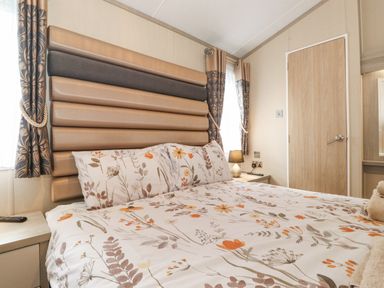 A bedroom with a bed with floral bedding a padded headboard bedside tables with lamp and curtains at Tawny Owl Lodge Coniston 4 White Cross Bay near Windermere