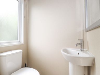 A bathroom with a toilet and a corner sink with a mirror above at Tawny Owl Lodge Coniston 4 White Cross Bay near Windermere