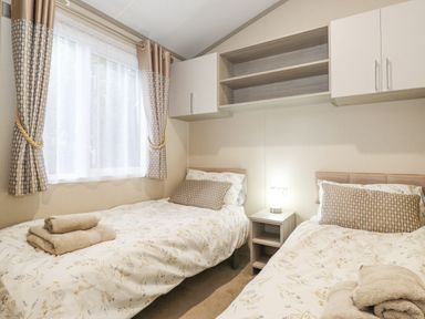 A bedroom with two single beds a window with curtains and a nightstand with a lamp at Tawny Owl Lodge in Coniston 4 White Cross Bay near Windermere