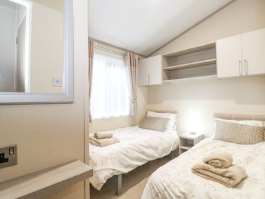 A bedroom with two single beds with floral bedding a nightstand with a lamp above storage cabinets and a window with curtains at Tawny Owl Lodge Coniston 4 White Cross Bay near Windermere