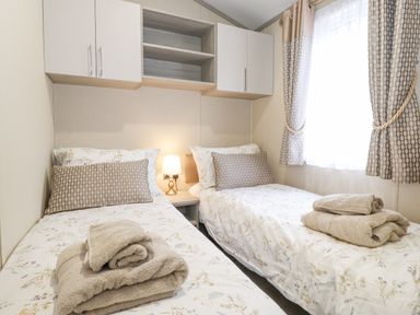 A bedroom with two single beds with folded towels a nightstand and wall cabinets at Tawny Owl Lodge in Coniston 4 White Cross Bay near Windermere