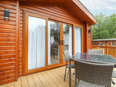 A wooden patio with glass door and table with four chairs at Tawny Owl Lodge in Coniston 4 White Cross Bay near Windermere