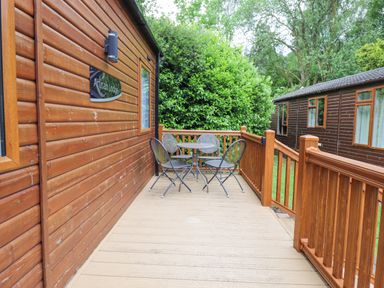 An outdoor wooden deck with a round table and four chairs attached to a wooden lodge at Tawny Owl Lodge Coniston 4 White Cross Bay near Windermere