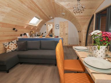 An arched wooden interior with a gray sofa orange chairs a dining table with plates and flowers and a kitchen area at Lapwing Chapel Le Dale near Ingleton