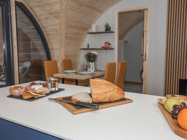 A kitchen island with bread and fruit trays and a dining table with plates and chairs at Lapwing in Chapel Le Dale near Ingleton
