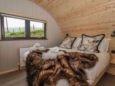 A bedroom with a double bed and animal print pillows and blanket and a window showing grassy outside at Lapwing in Chapel Le Dale near Ingleton