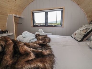 A bedroom with a bed covered with white sheets and fur blanket towels on bed and window on wall at Lapwing in Chapel Le Dale near Ingleton