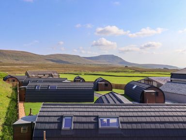 A group of pod-like buildings with dark roofs in a rural landscape with green fields and hills at Lapwing in Chapel Le Dale near Ingleton