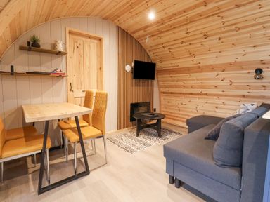 A living area with wooden walls a small dining table with chairs a gray sofa a small coffee table and a wall-mounted tv at Lapwing in Chapel Le Dale near Ingleton