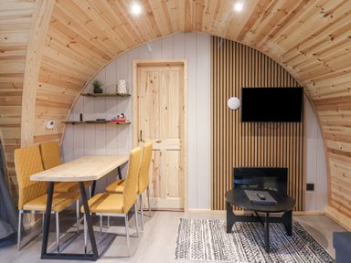 A small wooden room with a table and four yellow chairs a door shelves with books a wall-mounted tv and a small black coffee table at Lapwing in Chapel Le Dale near Ingleton