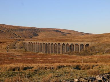 A stone railway viaduct with multiple arches in a hilly open landscape at Oyster Catcher in Chapel Le Dale near Ingleton