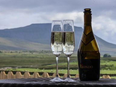 Two champagne flutes with bubbly drink and a bottle on a table with hills in the background at Oyster Catcher in Chapel Le Dale near Ingleton