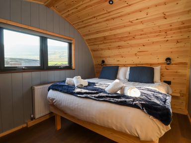 A bedroom with a double bed with towels on a navy blanket and wooden walls at Oyster Catcher in Chapel Le Dale near Ingleton