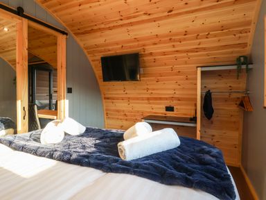 A bedroom with a bed and rolled towels a wall-mounted television an open wardrobe and a wooden ceiling at Oyster Catcher in Chapel Le Dale near Ingleton