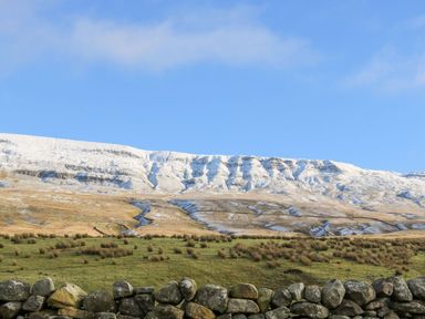 A landscape with a stone wall green grass brown hills and a snow covered ridge under a blue sky at Heron in Ingleton