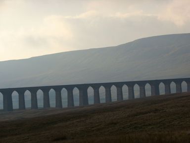 A stone railway viaduct with multiple arches across a grassy landscape with hills in the background at Heron Ingleton