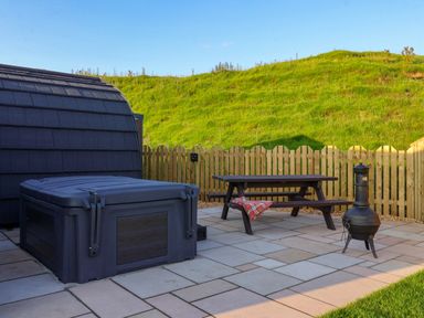 An outdoor patio with a covered hot tub a wooden picnic table with a blanket and a metal chiminea at Heron in Ingleton