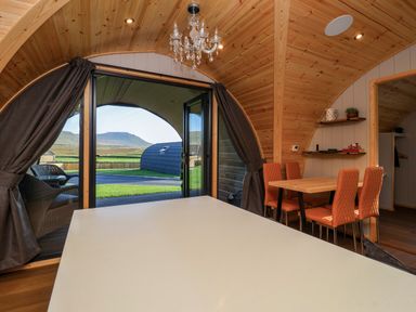 A wooden interior pod with a dining table and orange chairs next to open glass doors showing an outdoor view at Heron in Ingleton
