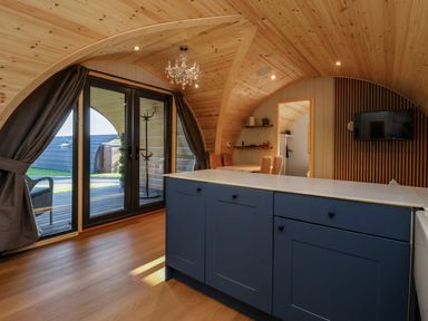 A wooden arched room with a kitchen island, dining table with chairs, chandelier, and glass doors at Heron in Ingleton
