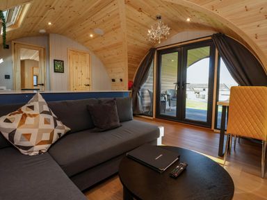 A living area with a gray sofa pillows a round black coffee table a chandelier and glass doors leading outside at Heron in Ingleton