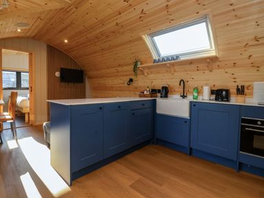 A kitchen with blue cabinets wooden walls and ceiling and a window above the sink at Heron in Ingleton