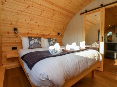 A bedroom with a bed with bird pillows and rolled towels next to a wooden mirrored door at Heron in Ingleton