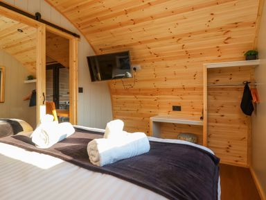 A bedroom with wooden walls a TV mounted on the wall towels on the bed and an open closet at Heron in Ingleton