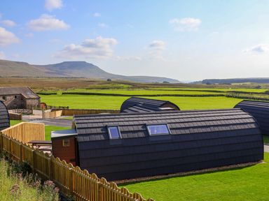 Curved roof cabins with skylights on green fields and mountains in the background at Heron Ingleton