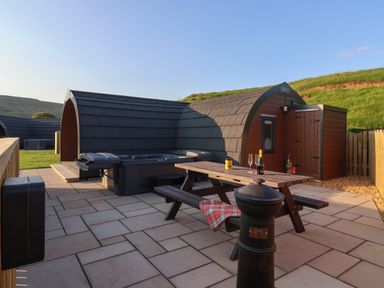An outdoor patio area with a wooden picnic table hot tub and pod cabin at Heron in Ingleton
