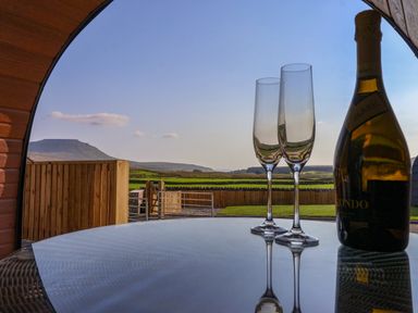 A table with two empty champagne glasses and a bottle with a countryside view through an arched window at Wren in Ingleton