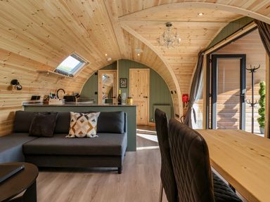A wooden interior room with a gray sofa a wooden dining table with black chairs and an open door to outside at Wren in Ingleton