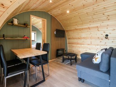 A small living area with a wooden dining table and black chairs next to a grey sofa and a mounted television at Wren in Ingleton