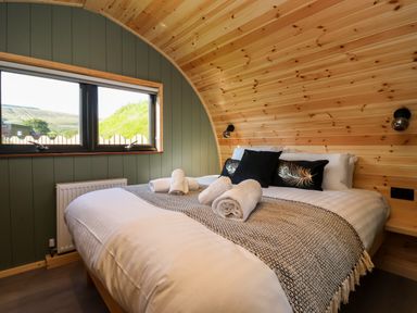 A bedroom with a bed with towels and pillows under a wooden arched ceiling at Wren in Ingleton