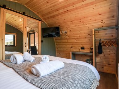A bedroom with a bed and rolled towels a wall-mounted tv a sliding door and a small open closet at Wren in Ingleton